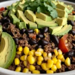 A colorful taco bowl with seasoned beef, rice, beans, corn, and fresh toppings.