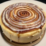A plated slice of Cinnamon Roll Cheesecake with icing drizzle.